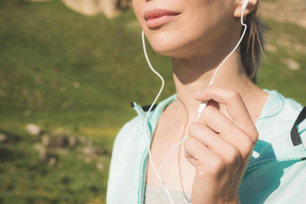 close-up of the bottom face of a young runner girl in nature before jogging. Chin and smiling lips of the sportswoman and hand on the microphone from the headphones - Photo, image