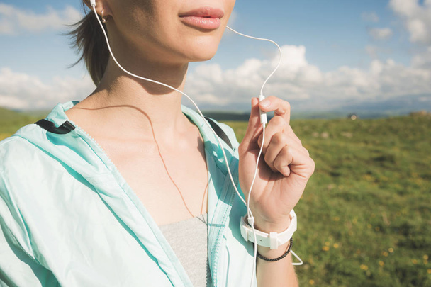 close-up of the bottom face of a young runner girl in nature before jogging. Chin and smiling lips of the sportswoman and hand on the microphone from the headphones - Fotoğraf, Görsel