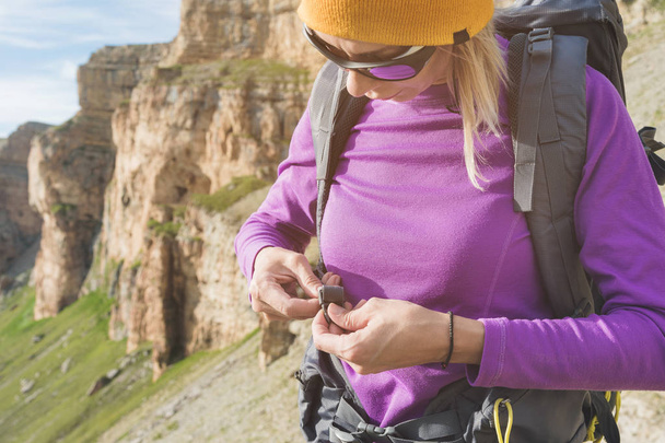 a tourist in sunglasses puts a backpack in the nature on the background of epic rocks preparing for trekking with climbing. The girl hiker fastens the fasteners on the backpack - Фото, зображення