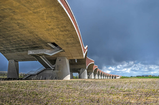 Με χάρη κάμπτοντας μπετόν και τούβλα καμάρες της νέας πόλης γέφυρα De Oversteek απέναντι στις πλημμυρικές περιοχές κοντά σε Nijmegen, Ολλανδία κάτω από τον σκυθρωπό ουρανό - Φωτογραφία, εικόνα