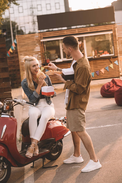 boyfriend feeding girlfriend with french fries near food truck  - Foto, afbeelding