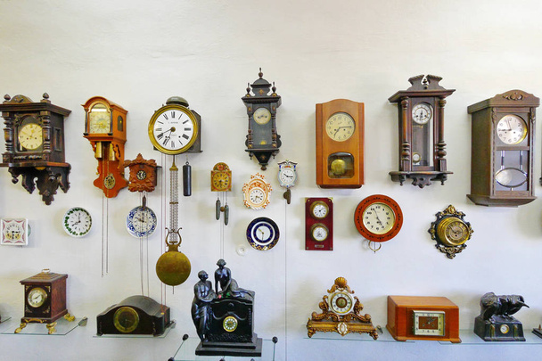 Μια συλλογή από αντίκες ρολόγια από διάφορα σχήματα και μεγέθη τοποθετούνται σε ένα λευκό τοίχο στις εγκαταστάσεις μουσεία. - Φωτογραφία, εικόνα