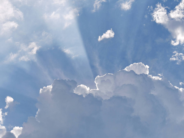 the rays of sunlight break through between the edges of a fluffy white cloud on a blue sky - Photo, Image