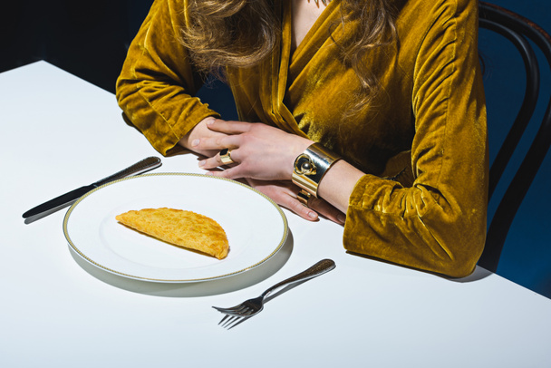 partial view of woman in luxury clothing sitting at table with meat cheburek on plate with blue backdrop - Foto, Imagem