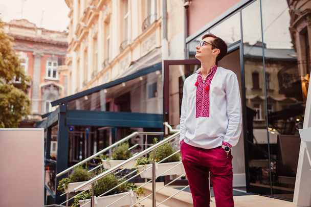 Nuori komea mies kävelee modernin kaupungin keskustassa. Ihminen käyttää perinteistä ukrainalaista paitaa
 - Valokuva, kuva