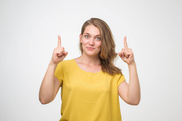 Femme européenne souriante en chemise jaune pointant le doigt vers le haut. Portrait isolé en studio
. - Photo, image