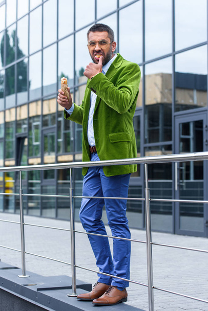 Zijaanzicht van de mens in groene fluwelen jas Franse hotdog eten op straat - Foto, afbeelding