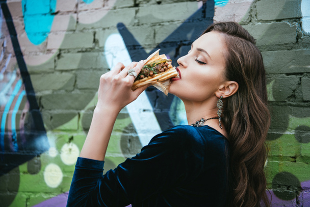 vista laterale di bella donna in abbigliamento elegante mangiare hot dog sulla strada
 - Foto, immagini
