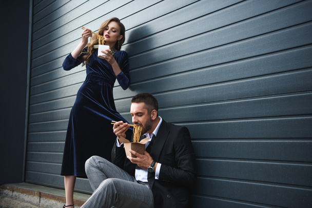 couple in fashionable clothing eating asian takeaway food on street - 写真・画像