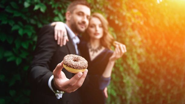 selective focus of fashionable couple with chocolate doughnuts with green foliage behind - Φωτογραφία, εικόνα