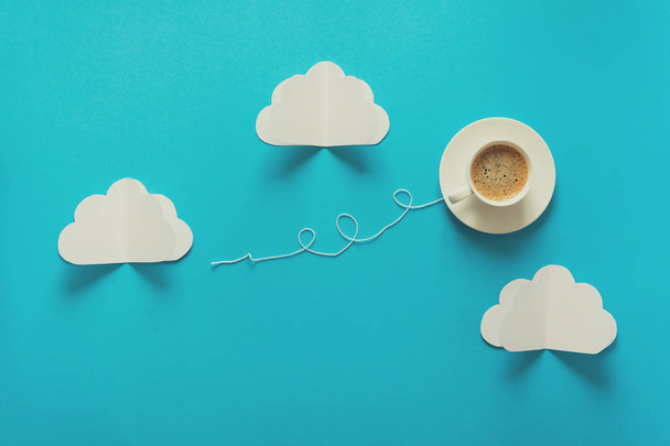 Coffee cup in shape of balloon with clouds on blue paper background. Toned - Φωτογραφία, εικόνα