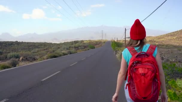 Matkustaja nainen liftaaminen aurinkoisella tiellä ja kävely. Backpacker nainen etsii kyytiä aloittaa matkan aurinkoisella maaseudulla tie
 - Materiaali, video