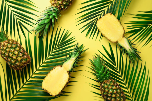 Pineapples and tropical palm leaves on pastel yellow background. Summer concept. Creative flat alay with copy space. Top view - Photo, Image
