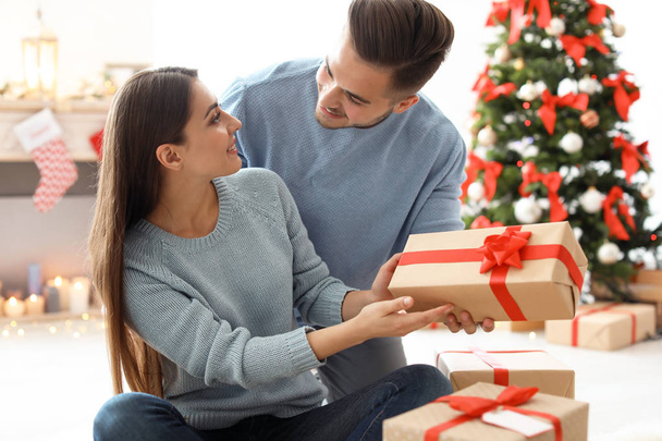 Young man giving Christmas gift to his girlfriend at home - Zdjęcie, obraz