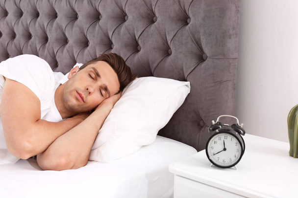 Fiatal férfi alszik az ágyban, és ébresztőóra éjjeliszekrényre otthon - Fotó, kép