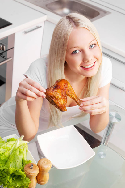 beautiful young blond woman eating fried chicken at home in the kitchen - Foto, Imagen