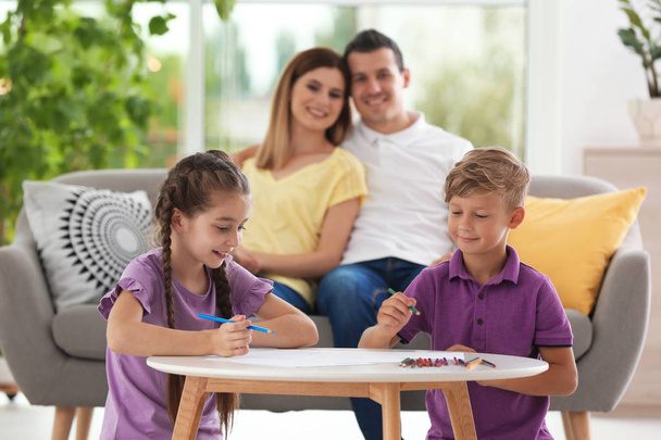Les enfants dessinent à table près des parents à l'intérieur. Famille heureuse
 - Photo, image