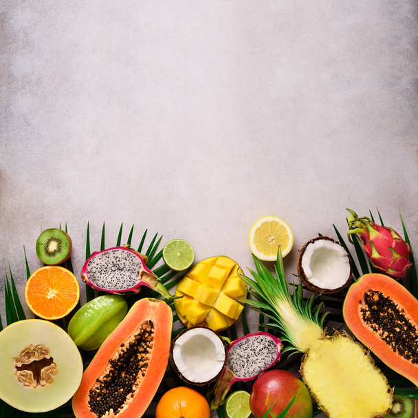 Exotic fruits and tropical palm leaves on grey concrete, background - papaya, mango, pineapple, banana, carambola, dragon fruit, kiwi, lemon, orange, melon, coconut, lime. Top view. - Foto, Imagen