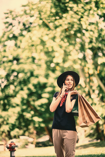 Porträt einer Frau, die ihr Smartphone benutzt und nach dem Einkaufen im Park steht. - Foto, Bild