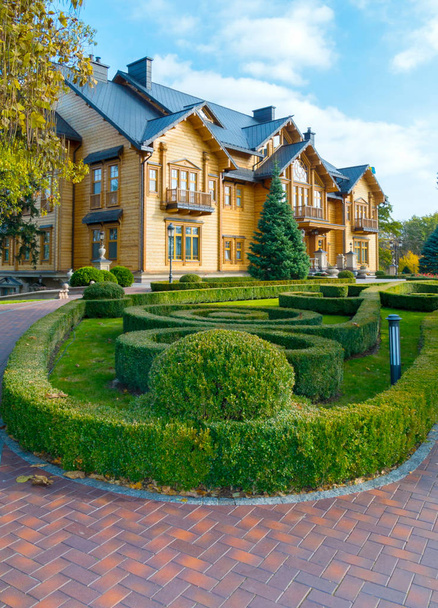 A flowerbed with a labyrinth of green bushes near the chic wooden mansion - Фото, зображення