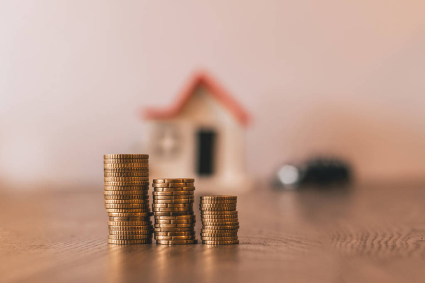 Coins stacked with a blurred house and car on the background: real estate, property investment, house mortgage, savings financial concept. - Fotoğraf, Görsel