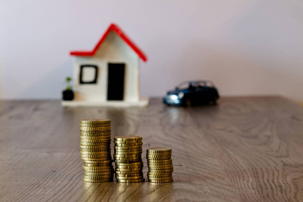 コインがぼやけている家と、背景に車、木製のテーブルの上に積み上げ: 不動産、不動産投資、住宅ローン、貯蓄金融の概念. - 写真・画像