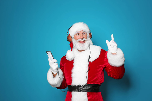Santa Claus listening to Christmas music on color background - Fotografie, Obrázek