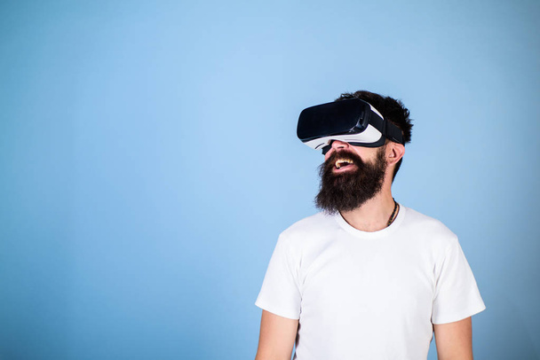 Hipster on smiling face enjoy virtual reality with gadget. Man with beard in VR glasses, light blue background. Digital technology concept. Guy with head mounted display interact in virtual reality - Foto, afbeelding