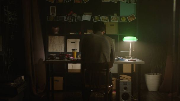 Κουρασμένος νεαρός άνδρας που εργάζεται με φορητό υπολογιστή στο σπίτι το βράδυ. Απόθεμα. Θλιβερή μοναχικός άνθρωπος που κάθεται στο τραπέζι στο σπίτι. Η έννοια της μοναξιάς - Φωτογραφία, εικόνα