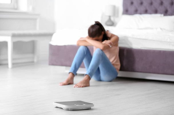 Schubben op de vloer en triest jonge vrouw thuis. Gewicht verlies motivatie - Foto, afbeelding