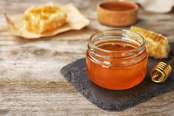 Glass jar with sweet honey and dipper on wooden table, closeup - 写真・画像
