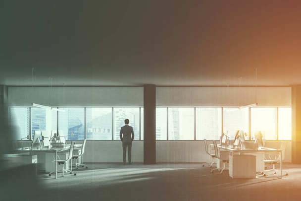 Бізнесмен стоїть у відкритому просторі лофт офісний інтер'єр з рядами комп'ютерних столів і білими стільцями, що стоять поруч. Чорні екрани комп'ютера. 3D візуалізація макет тоноване зображення подвійне експонування
 - Фото, зображення