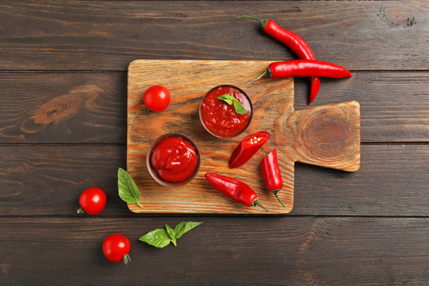 Flat lay composition with bowls of spicy chili sauce and cutting board on table - Fotoğraf, Görsel