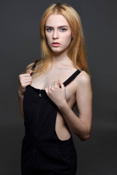 Portrait of the sexy beautiful woman with long red hair in black clothes posing in studio with grey background. - 写真・画像
