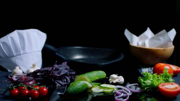 Still life of chef-cookers kitchen on the black mirror surface. Pan, knife, fresh vegetables and ingredientes for dish - Фото, зображення