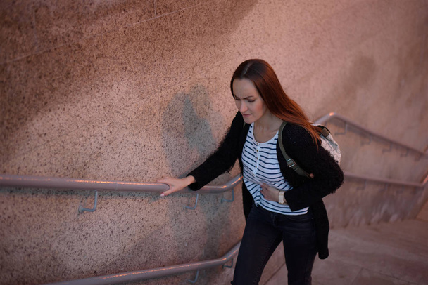 Portrait à mi-longueur de la vue du haut d'une jeune fille dans les escaliers du métro, la transition s'accroche à un estomac malade
. - Photo, image