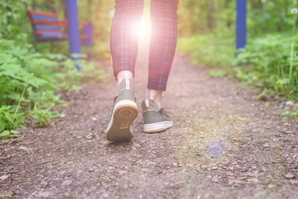 Slender female legs in plaid leggings and green sneakers go along the forest trail. Walks in the fresh air. - Fotoğraf, Görsel