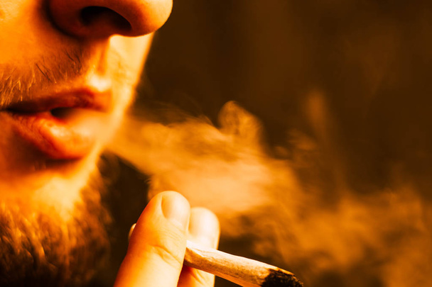 Cannabiskraut, einen Joint in der Hand, den ein Mann raucht. Rauch auf gelber Tonung - Foto, Bild