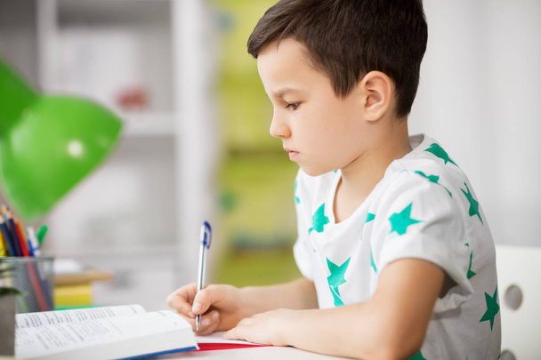 close up of boy with textbook writing at home - Foto, Bild