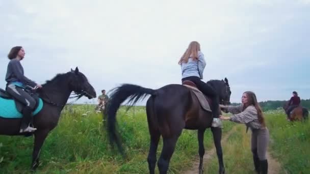 Nuori nainen auttaa ratsastajia suoristaa satula hevosen niityllä
 - Materiaali, video