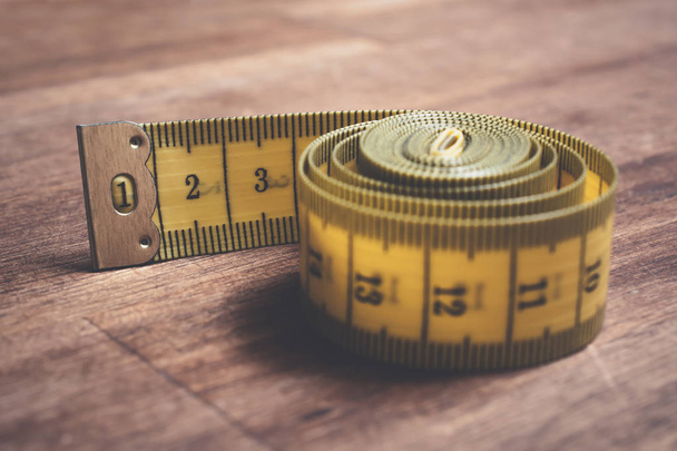 Macro de uma fita de medição amarela enrolada em uma mesa de madeira
 - Foto, Imagem