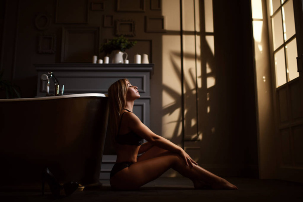 Young beautiful woman sitting in bathroom near expensive bathtub bath looking at the corner on dark  - Фото, зображення