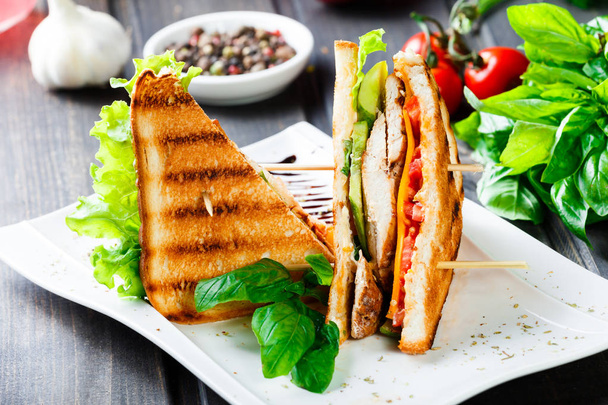 Club sandwich with cheese, cucumber, tomato, chicken meat and lettuce on dark wooden table. Delicious snacks, sandwiches, antipasti - 写真・画像