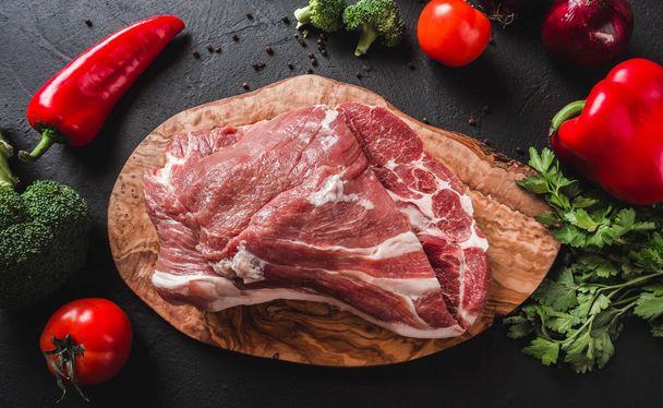 Nyers hús, marha steak, vágódeszka, fekete háttér összetevőket a főzéshez. Szemközti nézet - Fotó, kép