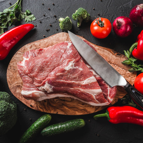 Viande crue, steak de bœuf sur planche à découper avec couteau sur fond noir avec des ingrédients pour la cuisson. Vue du dessus
 - Photo, image