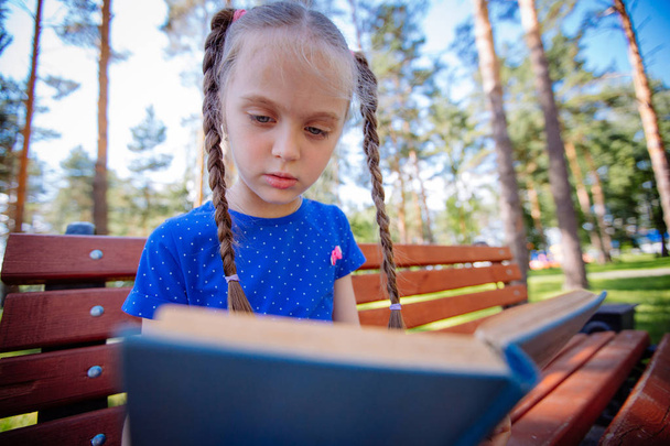 Cute little girl is reading a book outdoors - Fotoğraf, Görsel
