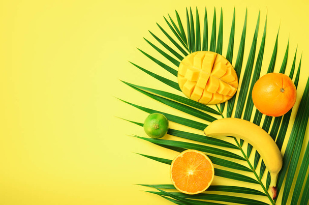 Fresh orange, banana, pineapple, mango smoothie and juicy fruits on palm leaves over yellow background. Detox summer drink. Vegetarian concept. Top view, flat lay, copy space - Foto, Bild