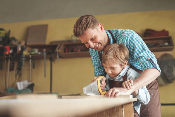 Pai e filho serrar uma prancha em carpintaria
 - Foto, Imagem