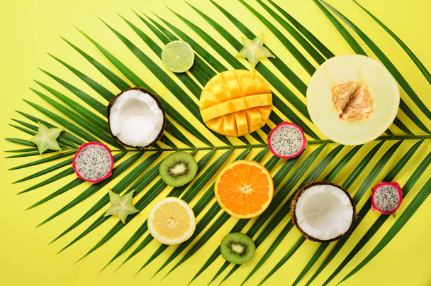 Exotic fruits and tropical palm leaves on pastel yellow background - papaya, mango, pineapple, banana, carambola, dragon fruit, kiwi, lemon, orange, melon, coconut, lime. Top view. - Foto, afbeelding