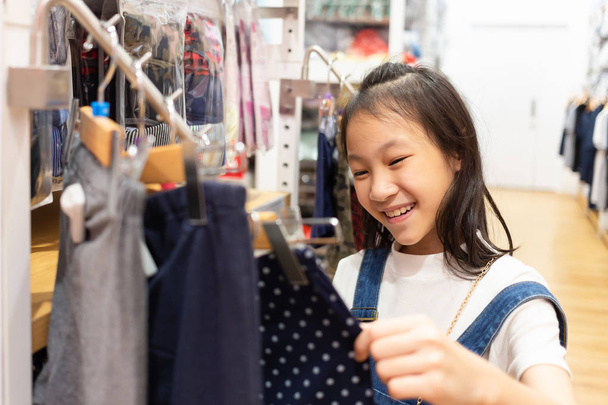 Happy Asian girl is choosing clothes in mall or clothing store,sale and consumerism concept - Photo, Image